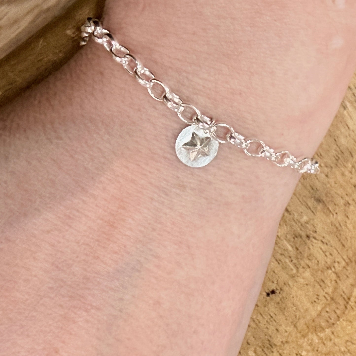 Silver bracelet with a star charm on a person's wrist against a wooden background