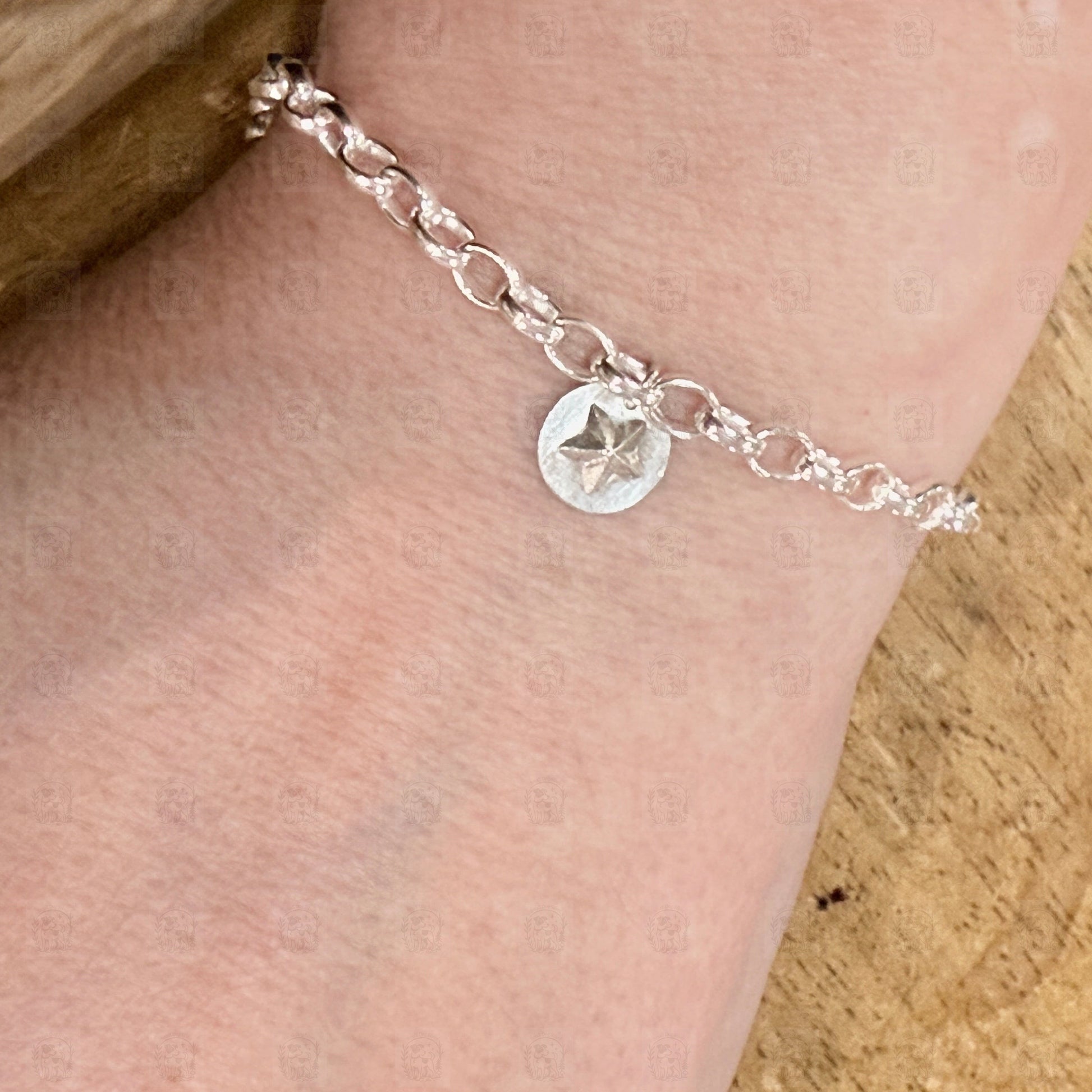 Silver bracelet with a star charm on a person's wrist against a wooden background