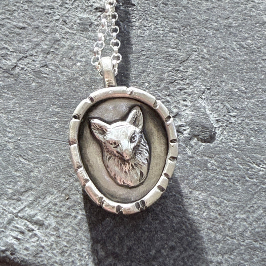 Silver fox pendant with a detailed design on a textured surface