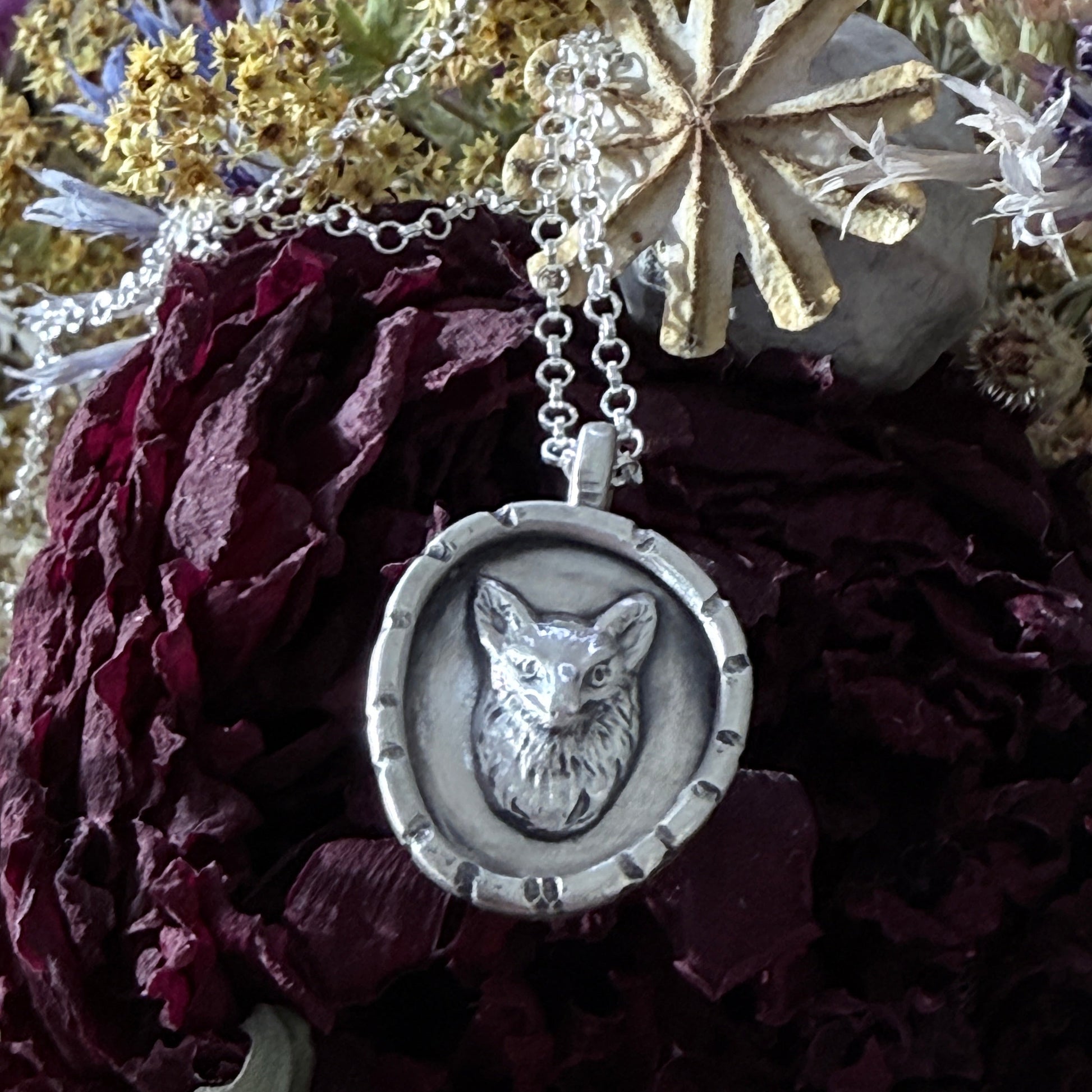 Silver necklace with a fox head pendant on a background of dried flowers