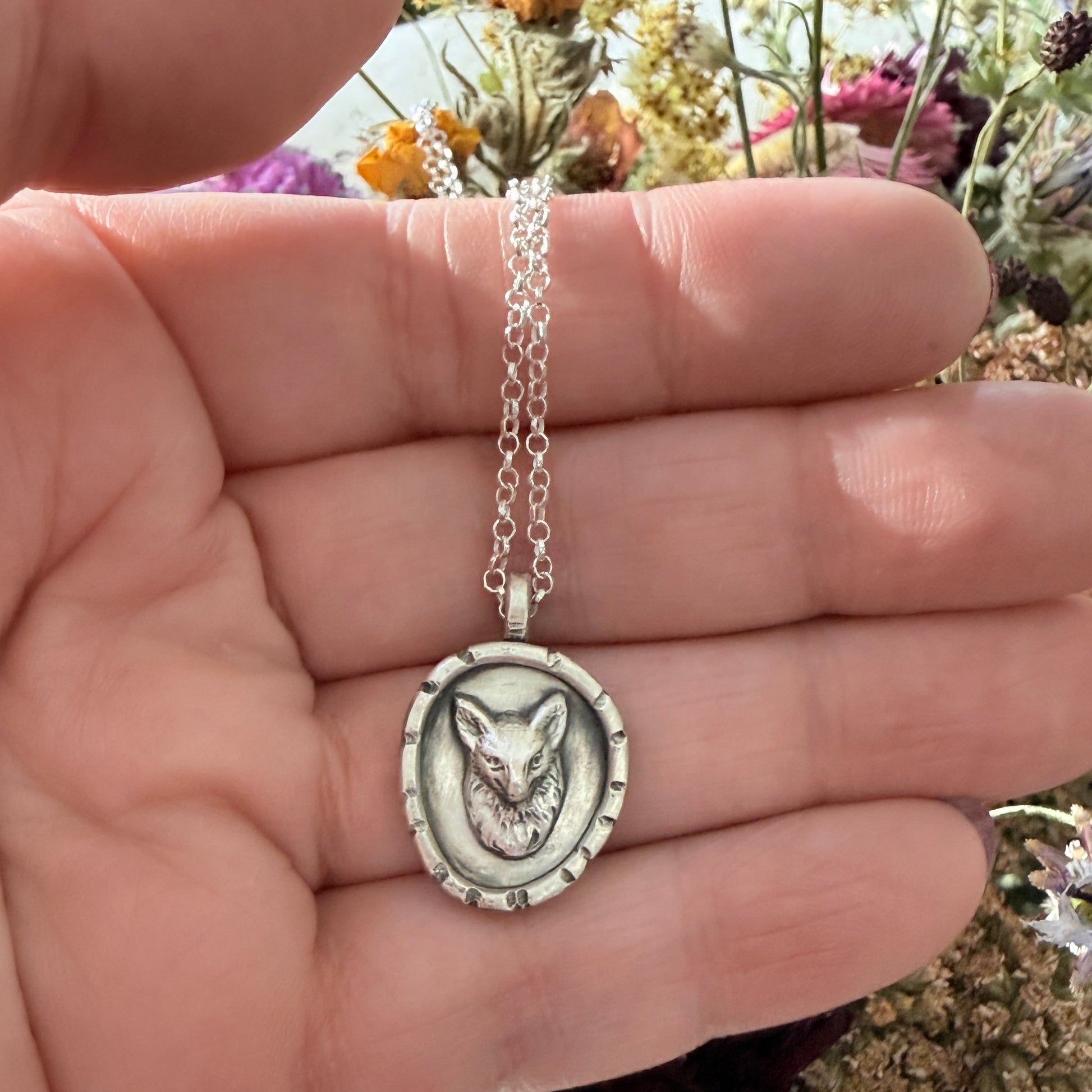 Silver necklace with a fox pendant held in a hand against a natural background