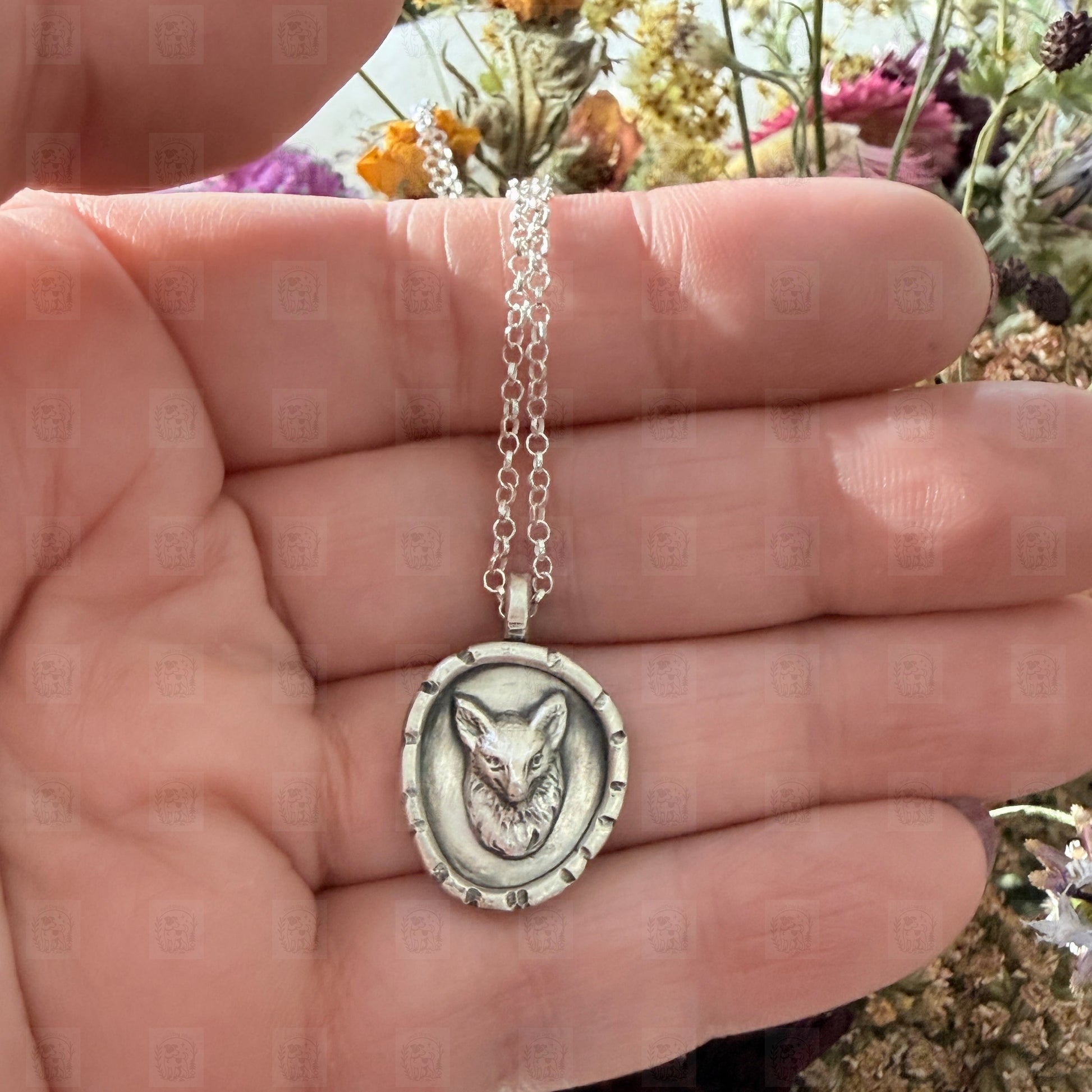 Silver necklace with a fox pendant held in a hand against a natural background