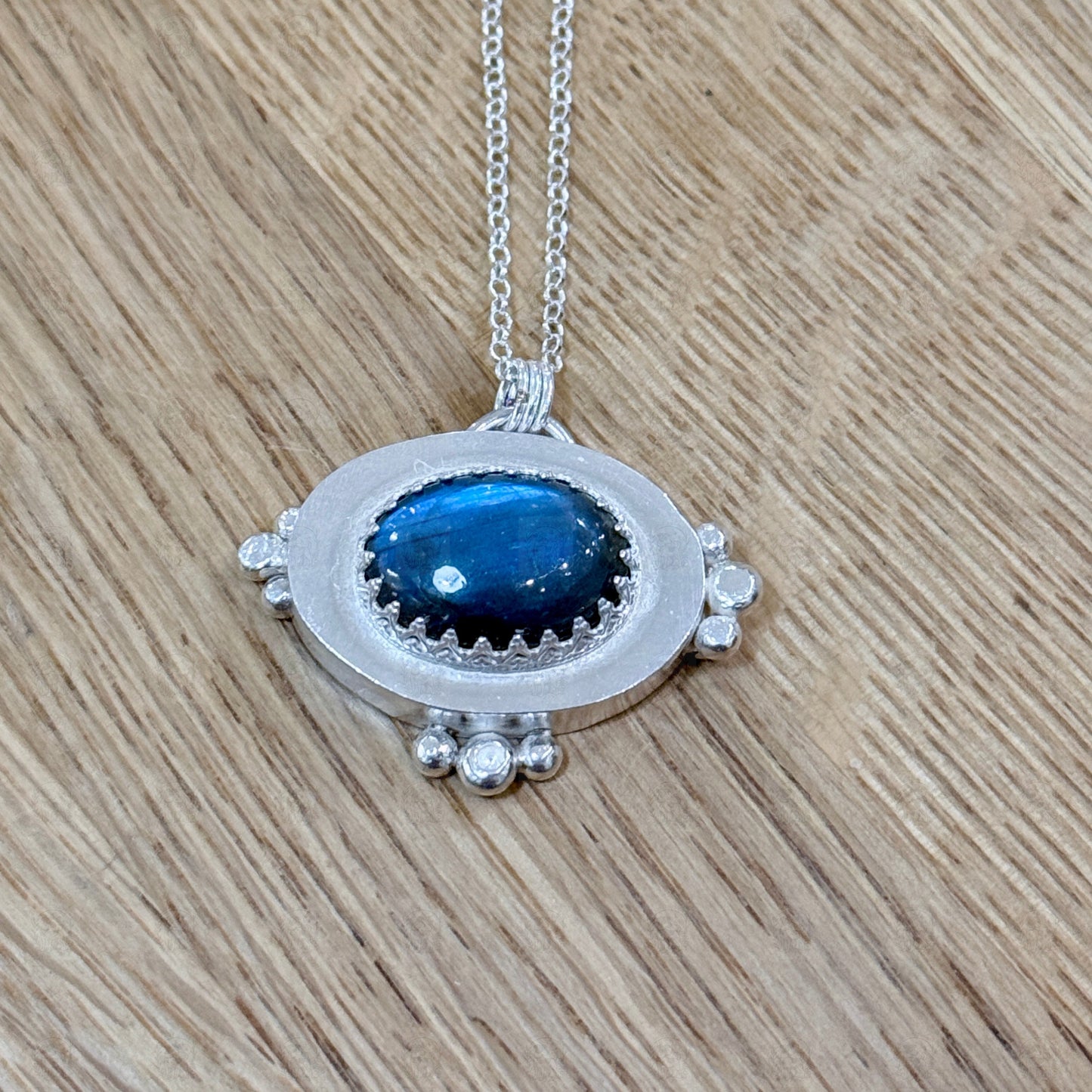 A sterling silver and labradorite pendant on a wooden background