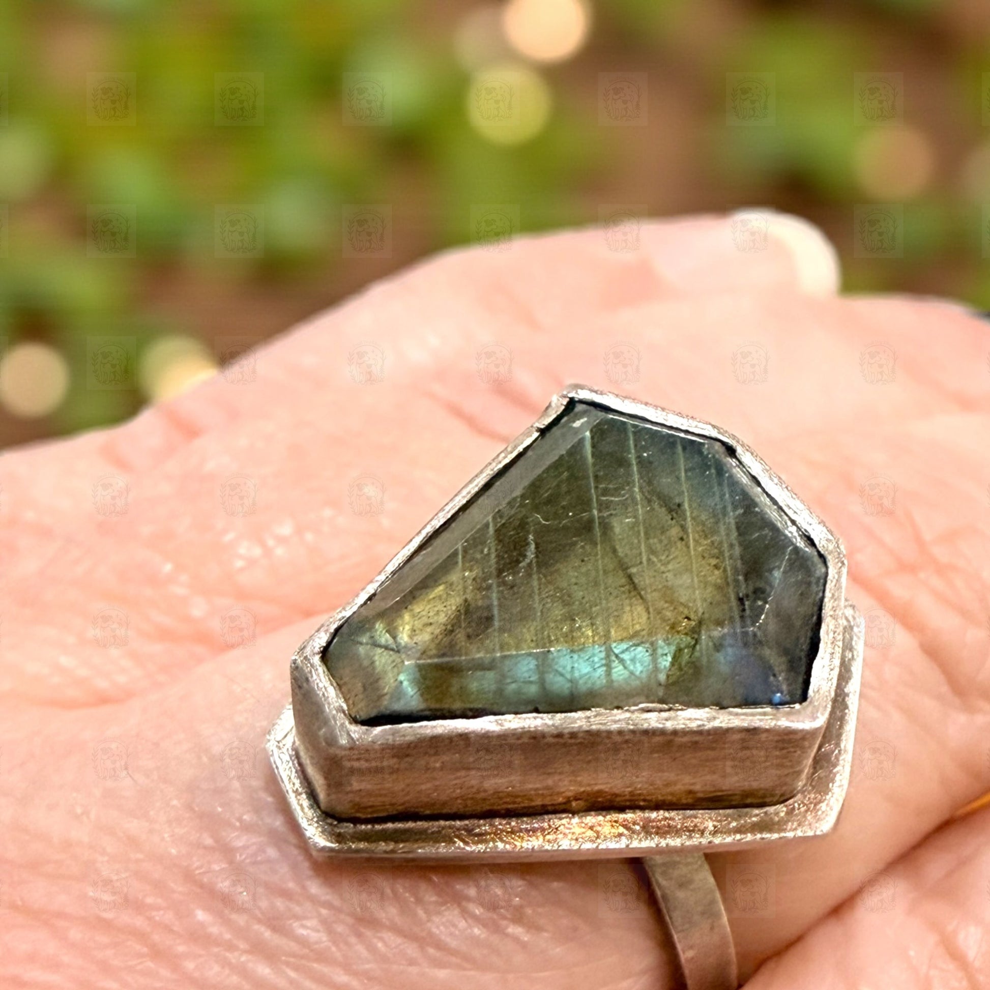 Labradorite ring with silver setting on a hand against a blurred natural background