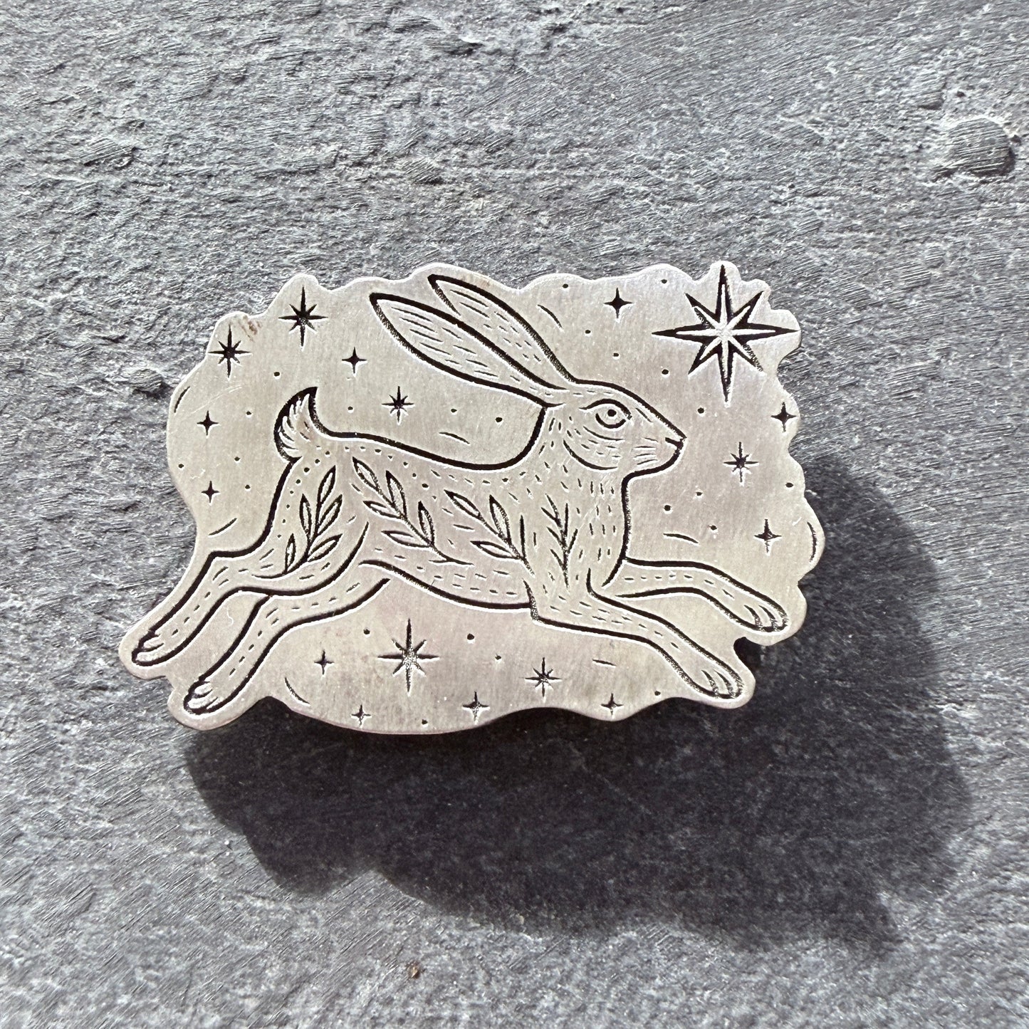 Sterling silver hare brooch with star and leaf design on a textured gray background