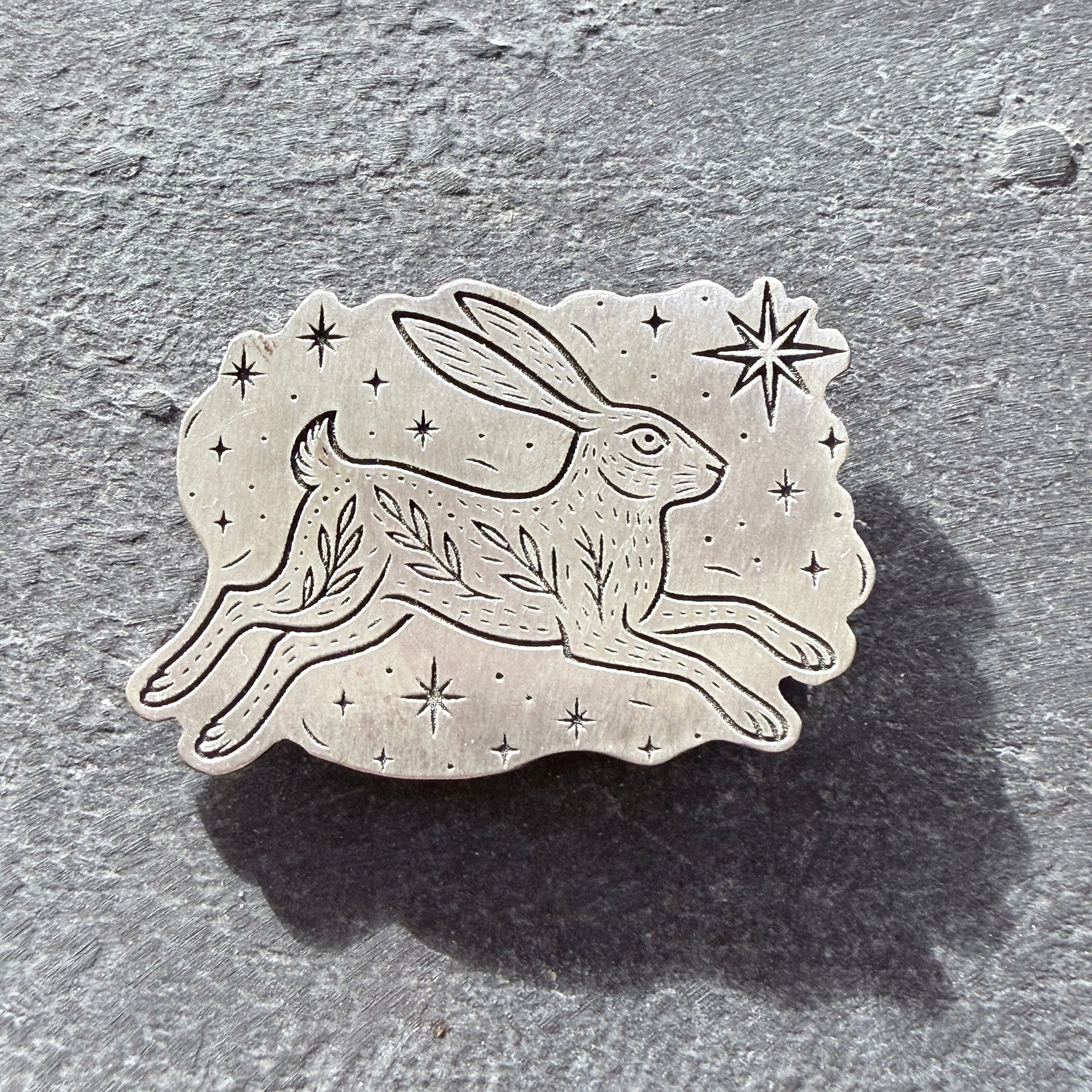 Sterling silver hare brooch with star and leaf design on a textured gray background