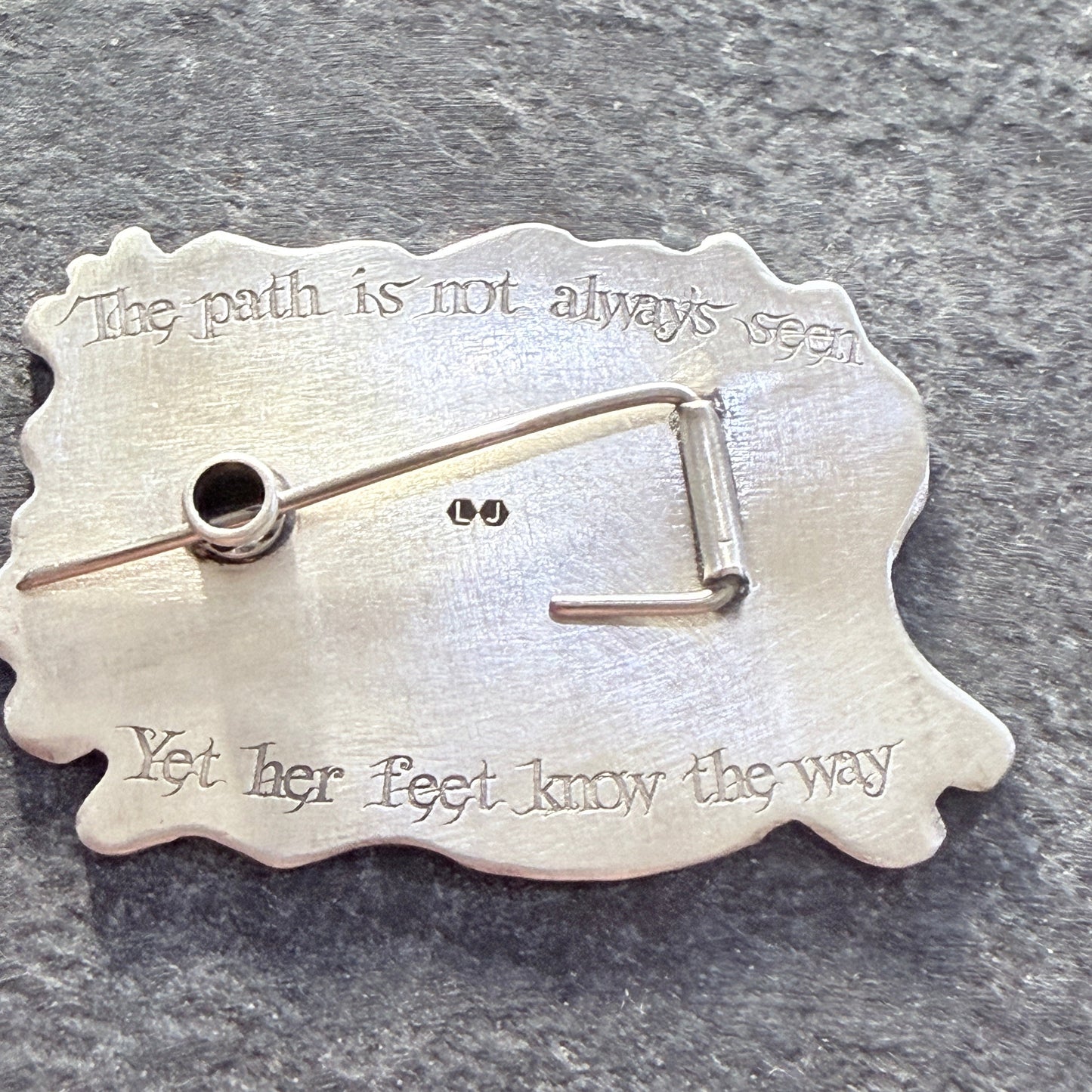 Silver brooch with engraved text on a gray background