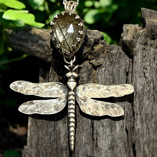 Dragonfly-shaped pendant on a chain against a natural background