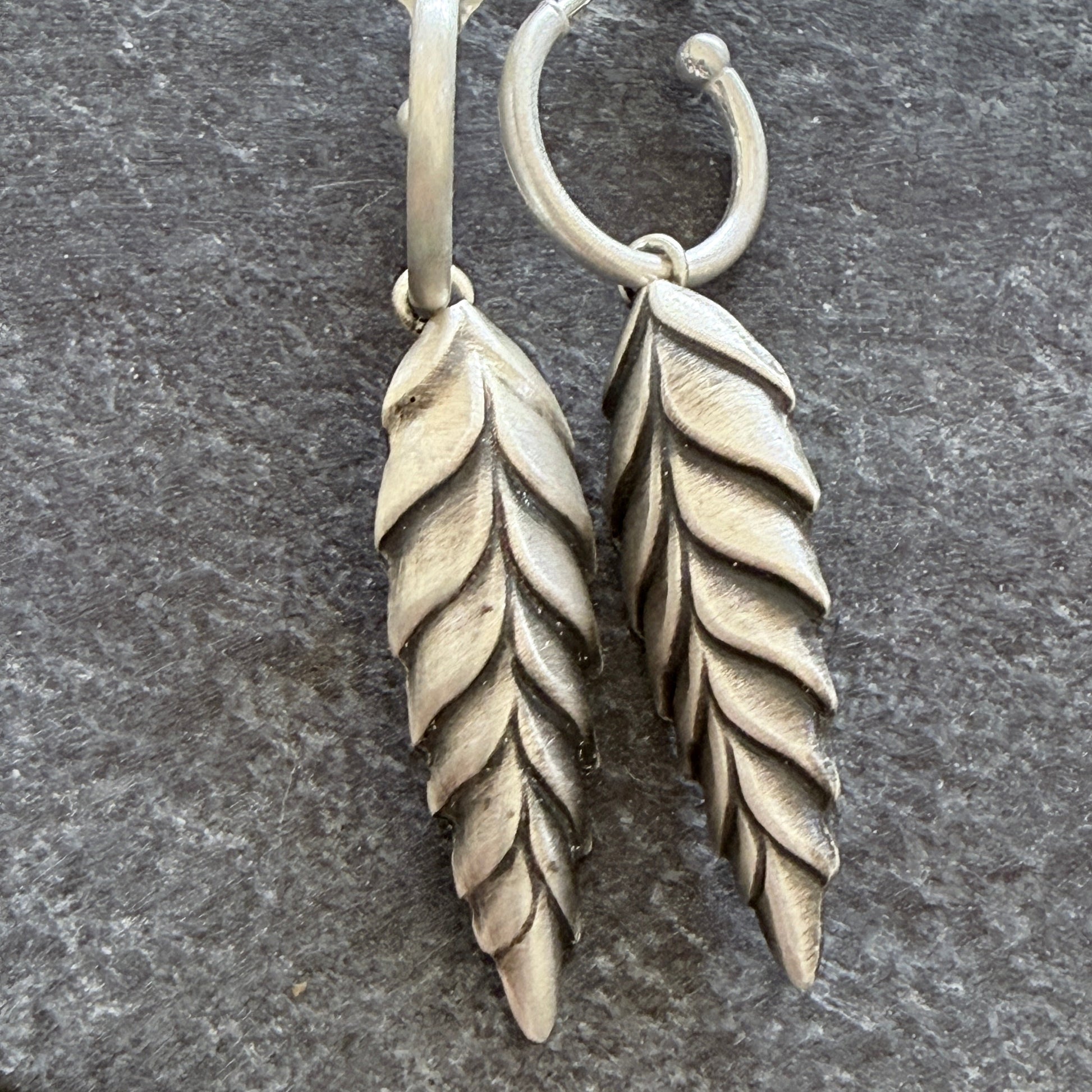 Pair of silver leaf-shaped earrings on a dark grey background