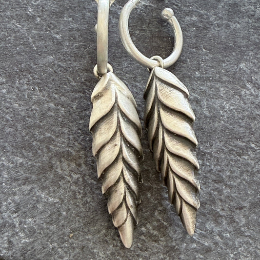 Pair of silver leaf-shaped earrings on a dark grey background
