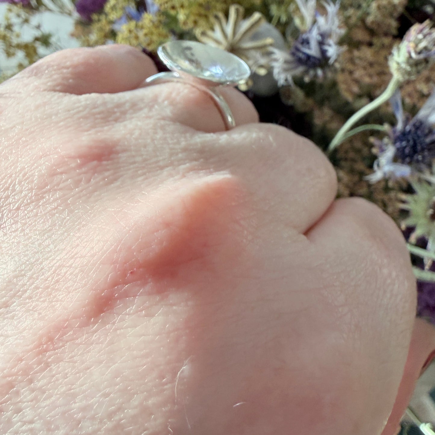 Close-up of a hand wearing a silver ring with flowers in the background