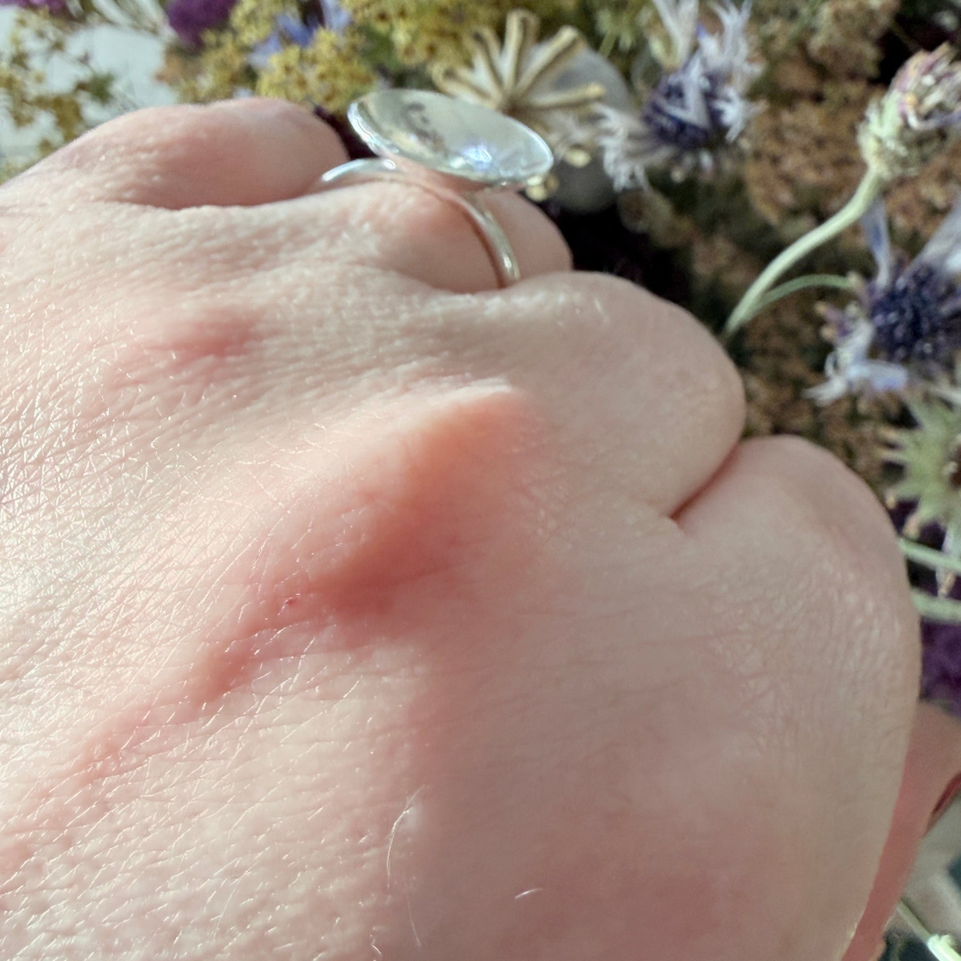Close-up of a hand wearing a silver ring with flowers in the background