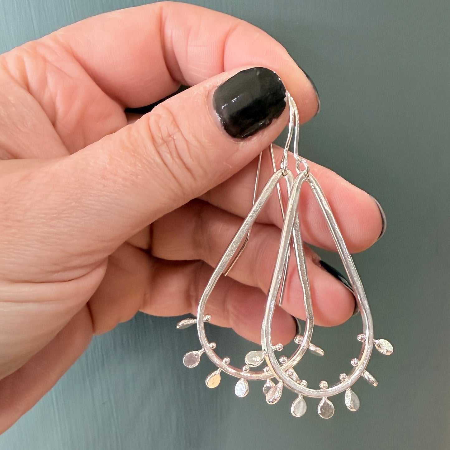 Hand holding silver teardrop earrings against a neutral background