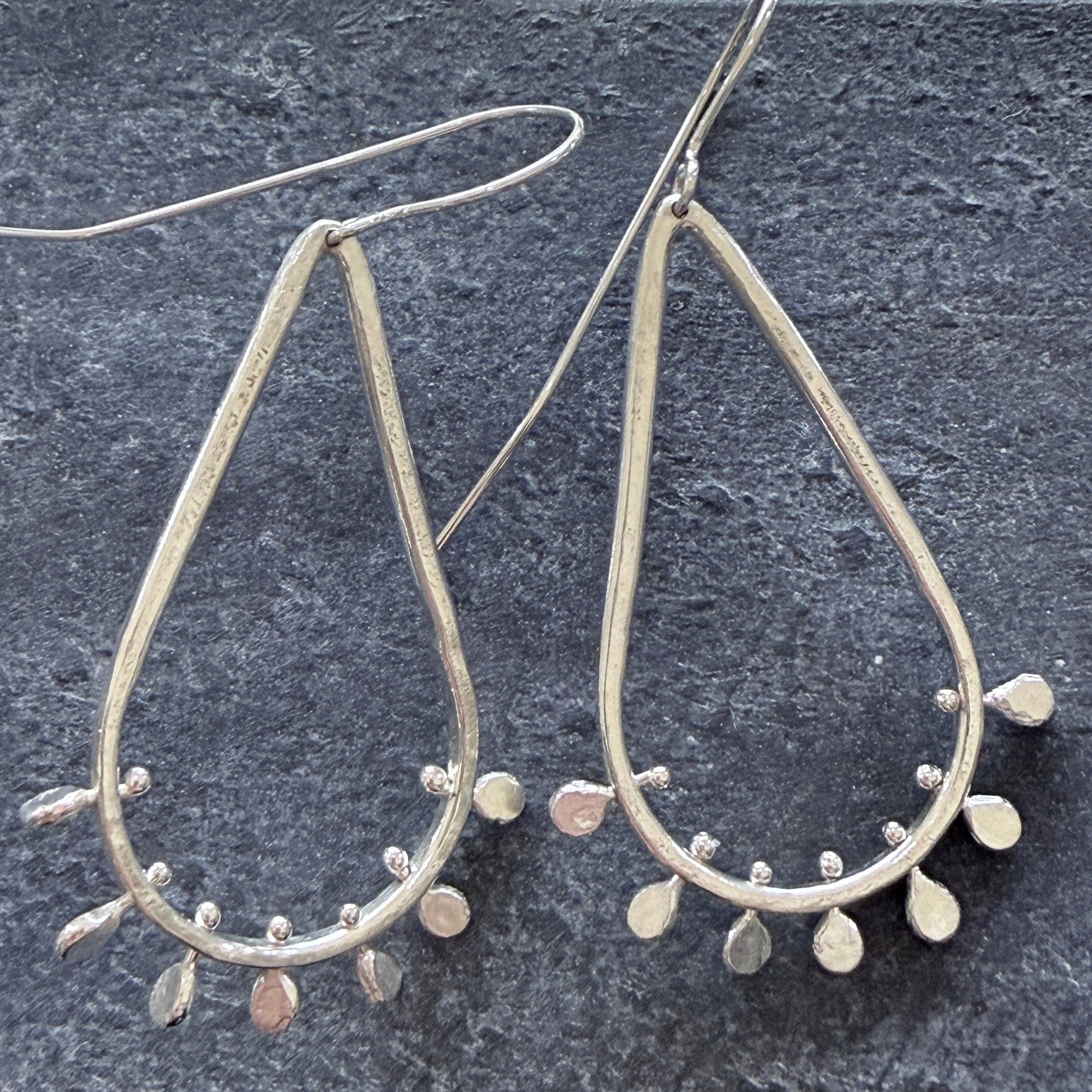 Silver teardrop earrings with paddle-like designs on a dark textured surface