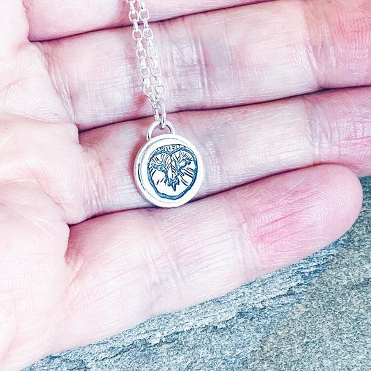 A sterling silver necklace with a round pendant featuring a barn owl design, held in a hand against a close-up background.